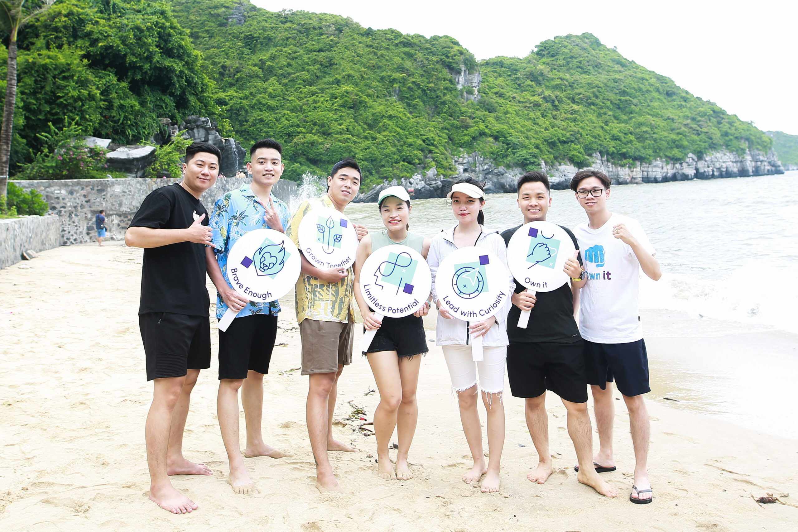 diverse group of people holding up XPON cultural values on a beach
